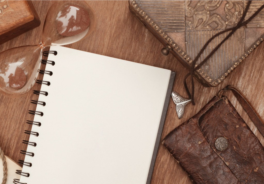 A notebook, necklace, and hourglass on a table.